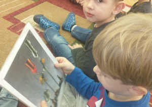 Chłopiec w niebieskiej bluzce ogląda na ilustracji wytwory z bursztynu